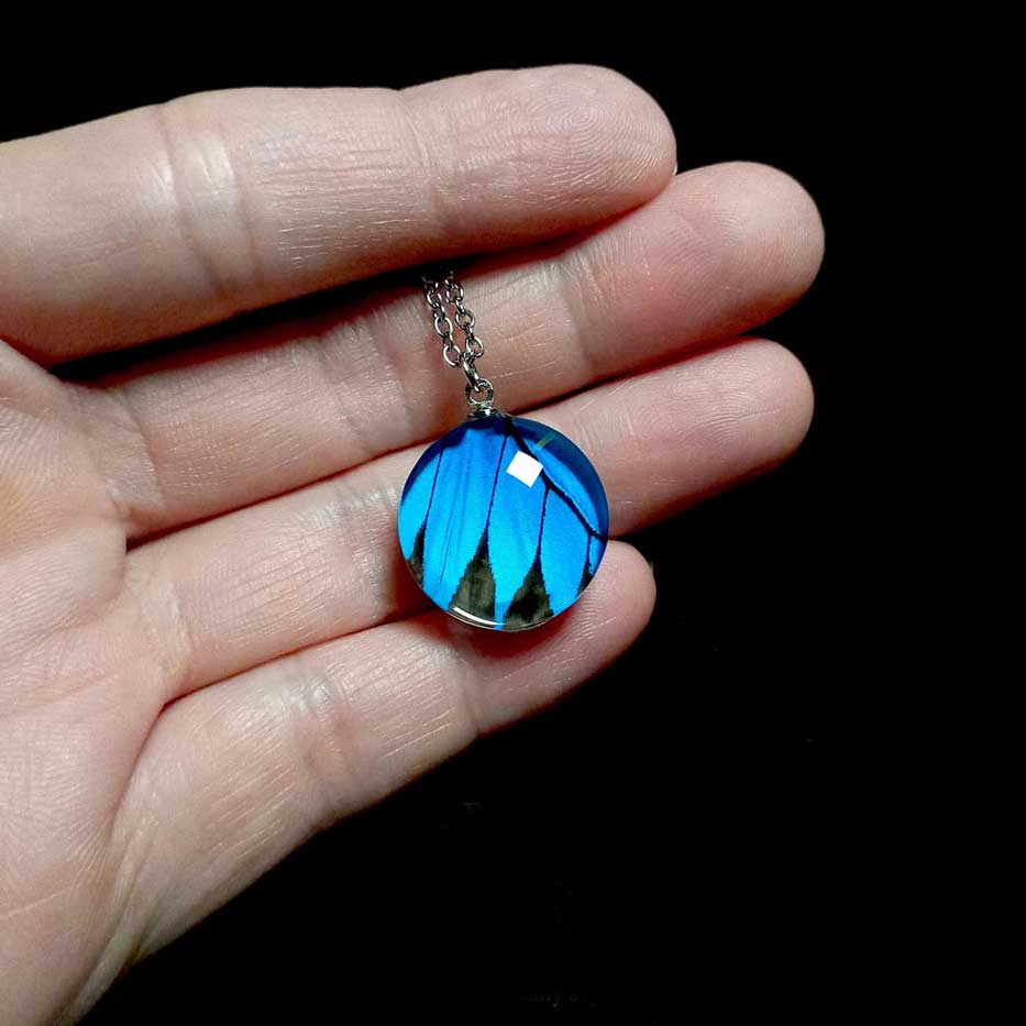 Collana con vera ala di farfalla Papilio ulysses mostrata sulla mano con ciondolo blu elettrico di farfalla macaone
