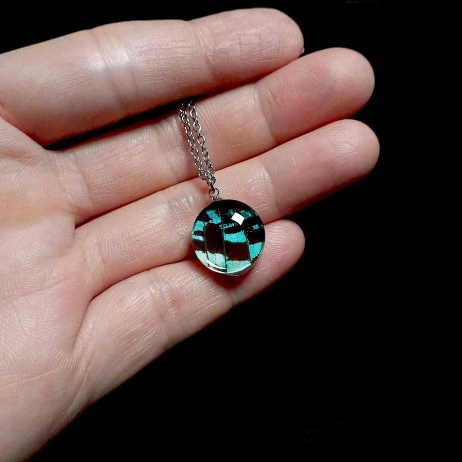 Collana con vera ala di falena Urania leilus mostrata sulla mano con ciondolo iridescente di falena diurna